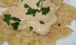 Pyszny makaron farfalle z kremowym sosem serowym, udekorowany świeżą natką pietruszki. Idealny na szybki obiad.