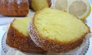Fette di ciambellone al limone spolverate di zucchero a velo, con limoni freschi sullo sfondo.