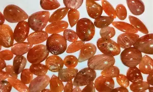 Mnóstwo błyszczących kamieni słonecznych o ciepłych, pomarańczowych odcieniach, ułożonych na białym tle.