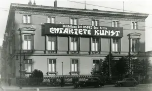 Große Banner verkünden die "Ausstellung der NSDAP Gau Berlin ENTTARTETE KUNST". Autos und Fahrräder stehen davor.
