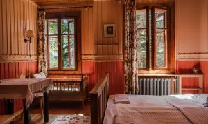 Przytulny pokój z widokiem na leśny ogród Lanckorona. Drewniane ściany, łóżko i stół tworzą sielski klimat.
