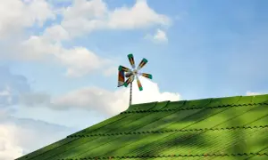 Piccolo impianto eolico domestico su tetto verde, con pale colorate che girano nel cielo azzurro con nuvole bianche.