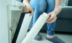 Osoba wymienia filtr w oczyszczaczu powietrza. Czy filtr HEPA można myć wodą? Zazwyczaj nie, ale warto sprawdzić instrukcję.