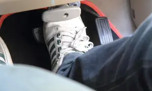Pédale de frein enfoncée, signe d'un symptôme de mauvaise purge frein. La chaussure blanche et jean bleu sont visibles.