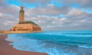 Wspaniałe maroko wakacje! Meczet Hassana II w Casablance nad turkusowym oceanem, z piaszczystą plażą i chmurami na niebie.