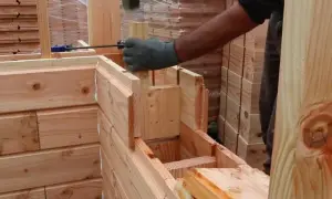 Construcción de una cabaña con madera aislante térmico. Un trabajador martilla una pieza de madera para encajarla.