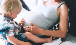 Liten pojke med blont hår känner på sin mammas mage, vecka 19.