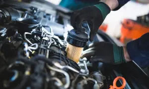 Mechanik w czarnych rękawiczkach wymienia filtr paliwa w silniku samochodu.