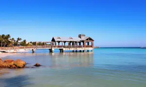 Un ponton en bois avec un kiosque, typique du parc Key West, s'avance sur une mer turquoise sous un ciel bleu éclatant.
