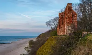 Ruiny kościoła w Trzęsaczu stoją na klifie nad Bałtykiem. W oddali pusta plaża i morze.
