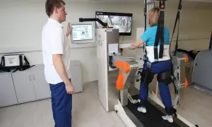Pacjentka w sanatorium z ZUS ćwiczy chód na bieżni w specjalistycznym egzoszkielecie, pod okiem fizjoterapeuty.