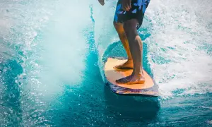 Mężczyzna na desce surfingowej, czując orzeźwienie wody, jak po użyciu perfum allure homme sport.
