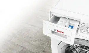 Szara podłoga i biała pralka Bosch z wysuniętą szufladą na detergenty. Dowiedz się, ile wody zużywa pralka.