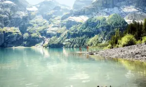 Zwei Personen genießen die Erfrischung in einem türkisfarbenen See vor majestätischen Schweizer Alpen.