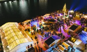 Buntes Treiben auf einem weihnachtsmarkt an der Spree. Menschen schlendern zwischen beleuchteten Buden und einem großen Weihnachtsbaum.