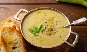 Una ciotola di calda crema di patate, guarnita con cipollotto fresco e pepe nero, servita con fette di pane tostato.