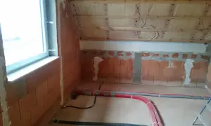 Neue Heizungsrohre verlegen im Rohbau. Rote und graue Rohre liegen auf dem Boden, bereit für die Installation.