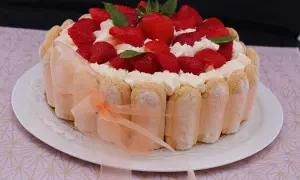 Charlotte aux fraises et fromage blanc, décorée de crème fouettée et de menthe fraîche. Un ruban pêche enlace le pourtour de biscuits à la cuillère.