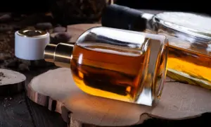 Elegancka butelka perfum o bursztynowym kolorze, sugerująca nuty wanilii i tytoniu, leży na drewnianym plastrze.
