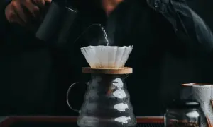 En person häller varmt vatten över kaffefilter för att brygga dropp kaffe. Ånga stiger från den nybryggda drycken.