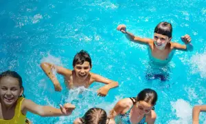 Niños riendo y chapoteando en una piscina azul, disfrutando del verano. ¡Una imagen perfecta de campamentos de inglés en España!