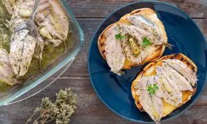 Alici al forno, profumate all'aglio e erbe, servite su crostini tostati e in una pirofila di vetro.
