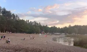 Plaża nad jeziorem w Jelczu-Laskowicach tętni życiem. Ludzie odpoczywają na piasku, kąpią się w wodzie, a dzieci bawią się przy dmuchanych zjeżdżalniach.