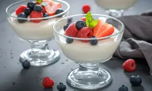 Två glas med krämig panna cotta, toppad med färska bär som jordgubbar, hallon och blåbär. En perfekt dessert.