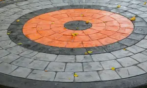 Kreisrunder Weg aus grau und orange gestrichenen Pflastersteinen, mit einigen Herbstblättern darauf.