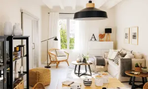 Salón luminoso con decoración de casas estilo nórdico moderno. Sofá beige, sillón de mimbre, mesa de centro redonda y estantería negra.
