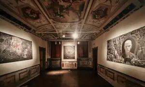 Sala di una galleria d'arte con soffitto affrescato e opere moderne. Le mostre ad Ancona presentano un'installazione con un volto stilizzato e un'opera astratta.