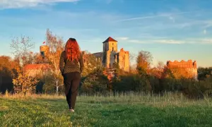 Kobieta z rudymi włosami idzie w stronę ruin zamku. To krajobraz inny niż krakowskie kopce, ale równie piękny jak trasy w Jurze Krakowsko-Częstochowskiej.