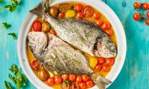 Orata all'acqua pazza, due pesci interi cotti in un brodo saporito con pomodorini e olive, guarniti con prezzemolo fresco.