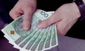 Dłonie trzymają stos banknotów 100 zł. To symbol dobrej stawki godzinowej, która pozwala na komfortowe życie.