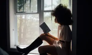 Vrouw met afro, zittend bij het raam met een boek, diep nadenkend over haar relatie.