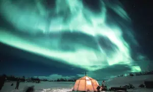 Ein beleuchtetes Zelt unter dem Nordlicht in verschneiter Landschaft.