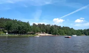 Spokojne jezioro Stobno otoczone zielonym lasem, z plażą i kilkoma łodziami.