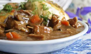 Gęsty gulasz z grzybami suszonymi i kawałkami mięsa, podany z pieczywem i posypany koperkiem.