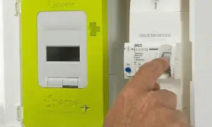 Main d'un homme actionnant un disjoncteur de type BACO en position OFF, à côté d'un compteur Linky vert.