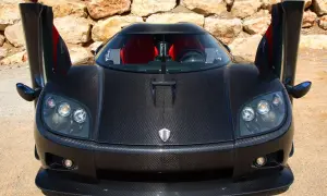 Czarny Pagani z otwartymi drzwiami, wykonany z włókna węglowego, z czerwonymi siedzeniami, na tle kamiennej ściany.