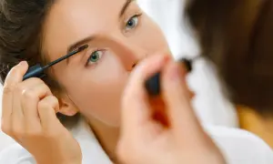 Une femme applique du mascara sur ses sourcils, préparant son maquillage bagage cabine pour un voyage.