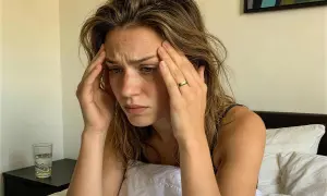 Woman with hands on temples, looking distressed in bed. She's experiencing insomnia before her period, a common struggle.