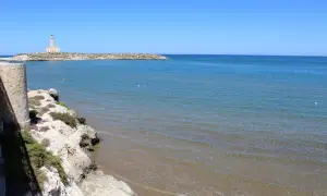 Faro di Vieste, Stella Maris, su un'isola rocciosa con mare azzurro e spiaggia sabbiosa.