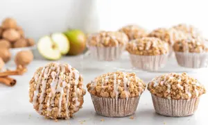 Leckere Apfelmuffins mit Streuseln und Zuckerguss, perfekt für ein Apfelmuffins Rezept. Daneben liegen Äpfel und Zimtstangen.