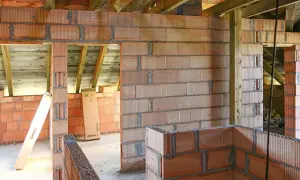 Budowa domu z bloczków z betonu komórkowego. Widać ściany z pustaków, drewniane belki stropowe i materiały budowlane, jak klej czy zaprawa do betonu komórkowego.