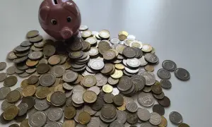 Różowa świnka-skarbonka i stos monet. Zastanawiasz się, ile kosztuje konsultacja u prawnika? Może warto zacząć oszczędzać?