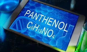 Tablet z napisem PANTHENOL i wzorem chemicznym C9H19NO4, otoczony probówkami z zielonym płynem i elementami chemicznymi.