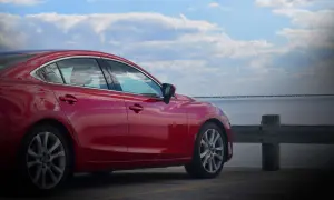 Czerwona Mazda 6 2.0 benzyna zaparkowana nad wodą, z mostem w tle.