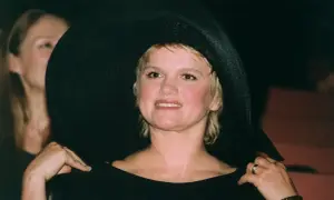 Kobieta w czarnym, szerokim kapeluszu i czarnej bluzce, uśmiecha się.