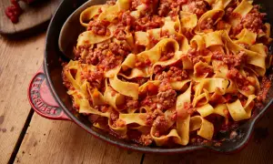 En stor portion krämig pasta bolognese i en röd gjutjärnspanna.